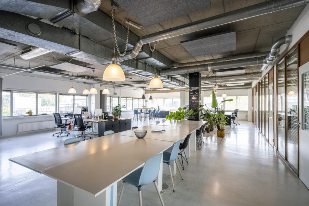 Moderne, open kantoorruimte aan de Anthony Fokkerweg met lange werktafels, bureaus, veel daglicht en groene planten.